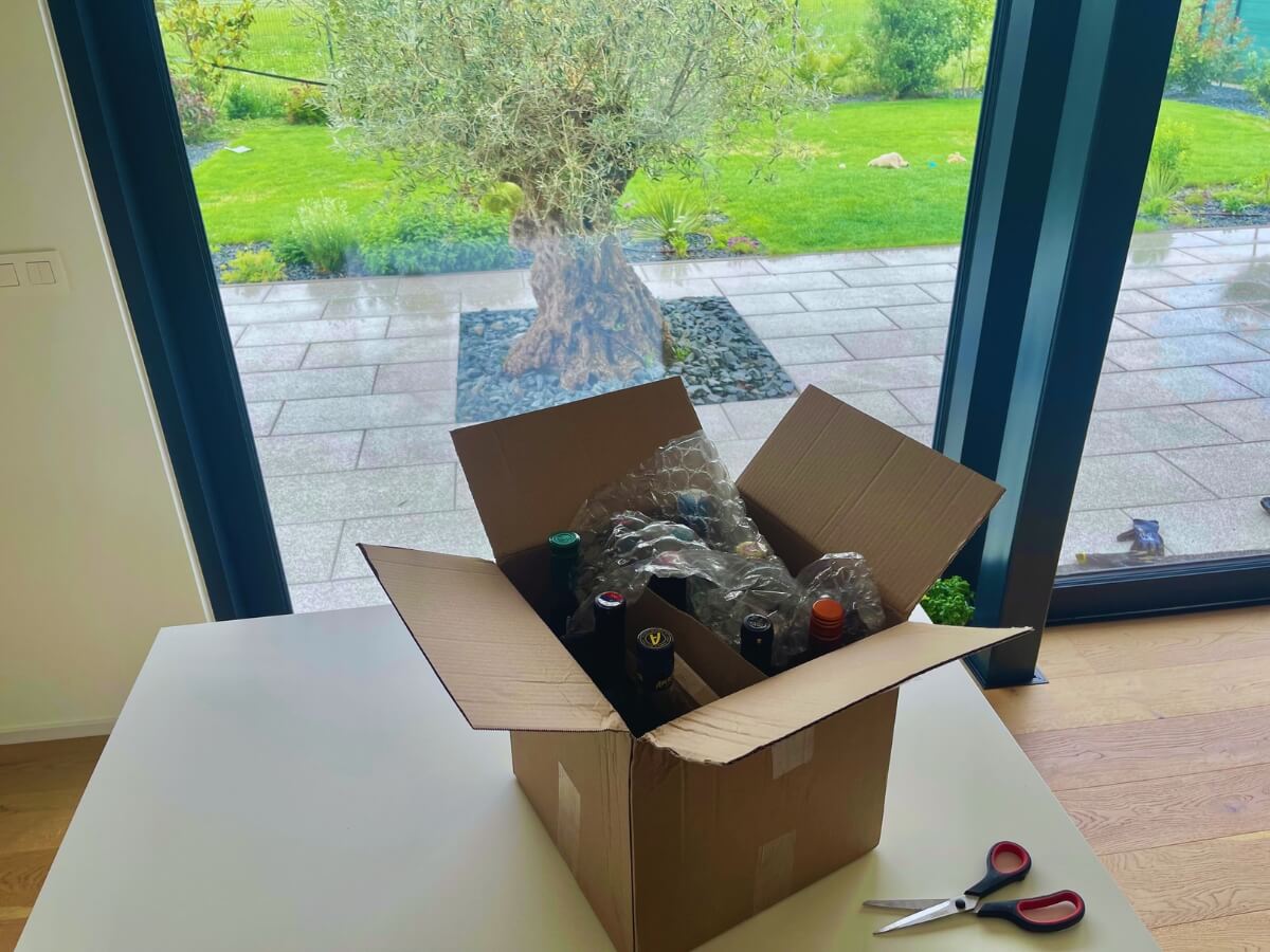 Rozbalený balík se skleněnými lahvemi položený na kuchyňské desce, v pozadí zahrada.