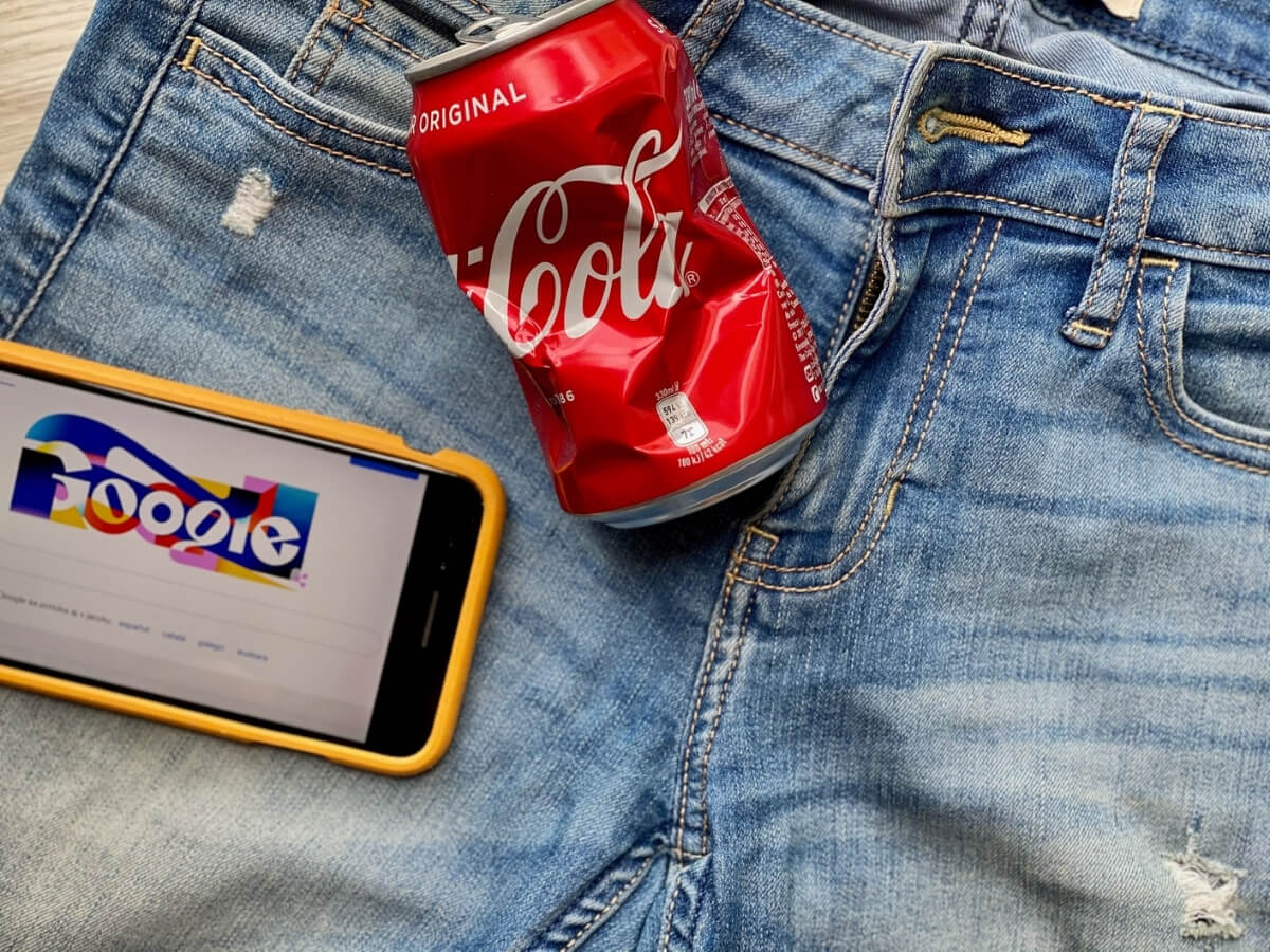 Plechovka Coca Coly a mobil s otevřeným vyhledávačem Google položené na riflích.