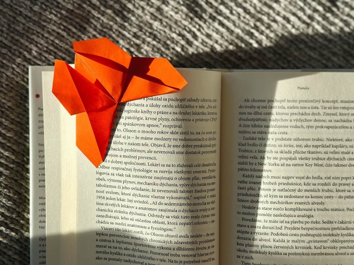 Oranžová záložka ve tvaru origami motýla v knize.